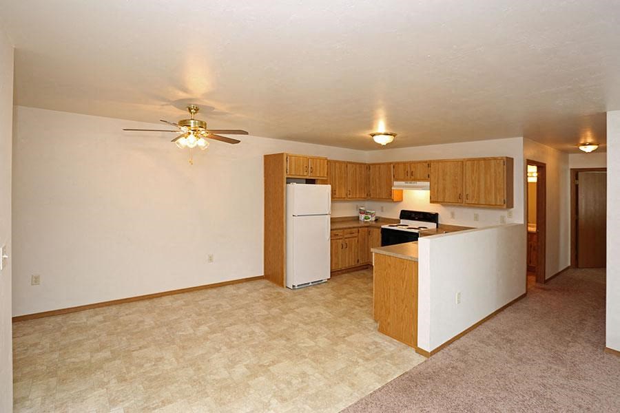 an empty living room with a kitchen and a ceiling fan