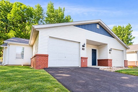 A two-car garage with a brick pillar and a black door is situated in front of a house.