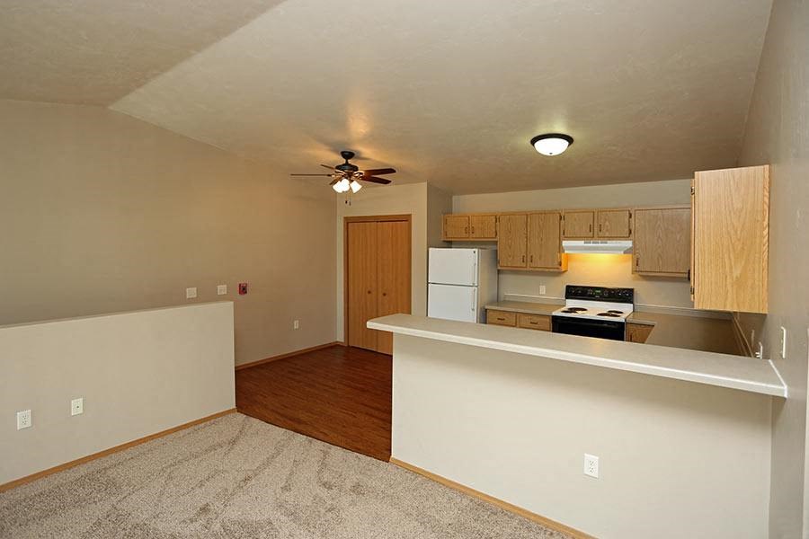 an empty living room with a kitchen and a ceiling fan