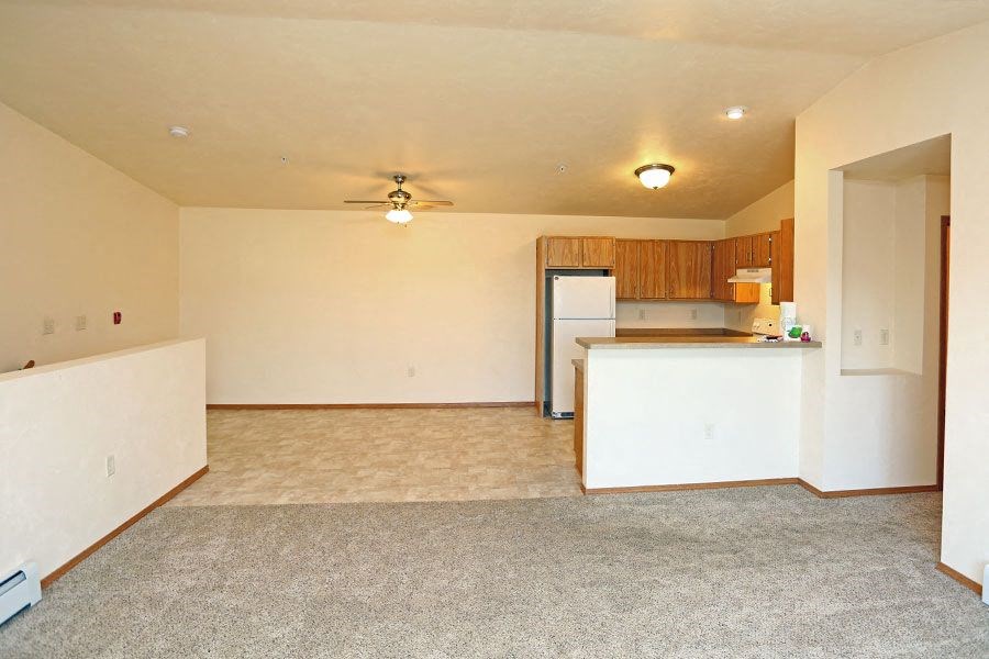 an empty living room with a kitchen and a ceiling fan