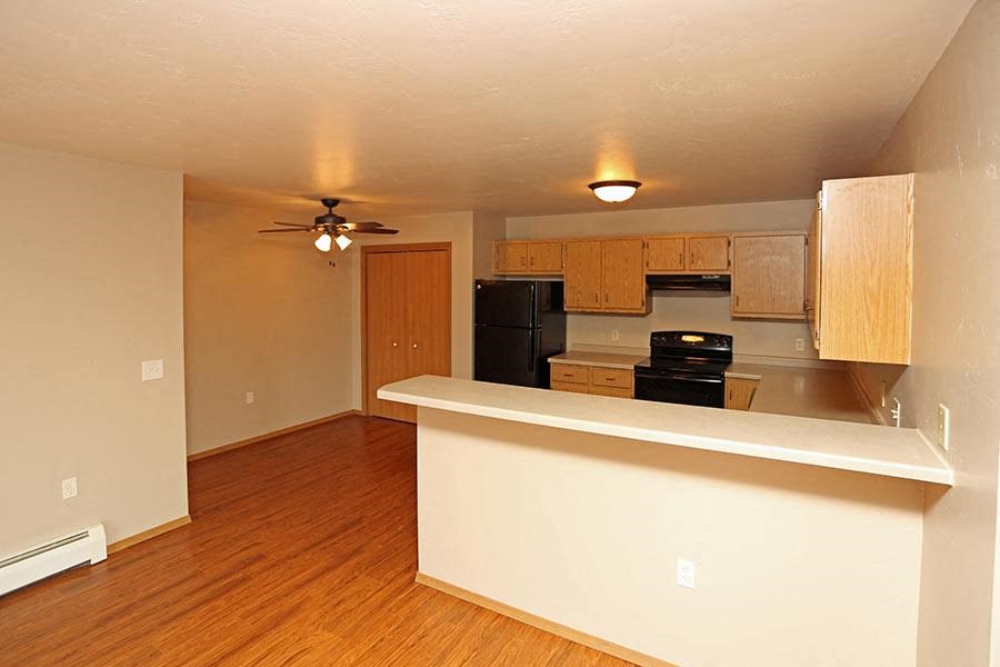 an empty living room with a kitchen and a ceiling fan
