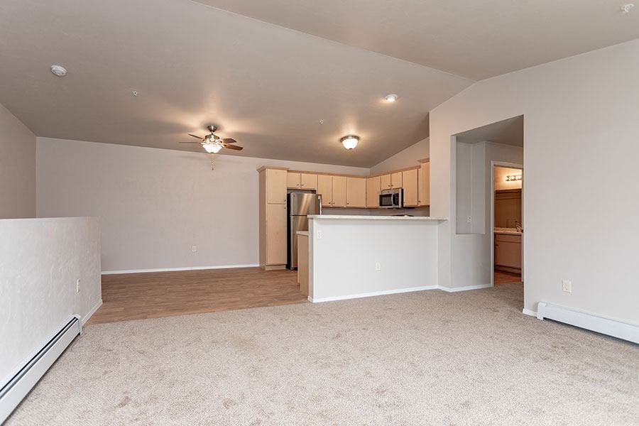 an empty living room with a kitchen and a ceiling fan