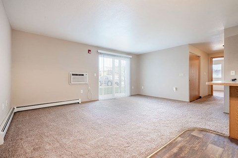 an empty living room with a kitchen and a window
