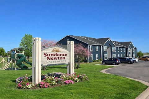 A sign for Sudance Newton Apartments stands in front of a building.