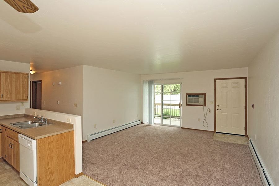 an empty living room with a kitchen and a door