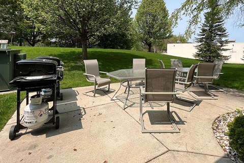 A black grill is on a patio with four chairs.