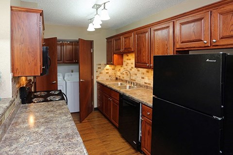A kitchen with a black refrigerator, wooden cabinets, and a granite countertop.