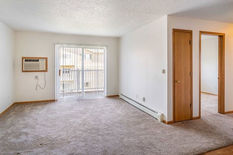 A room with a carpeted floor, a door, and a window with a view of a balcony.