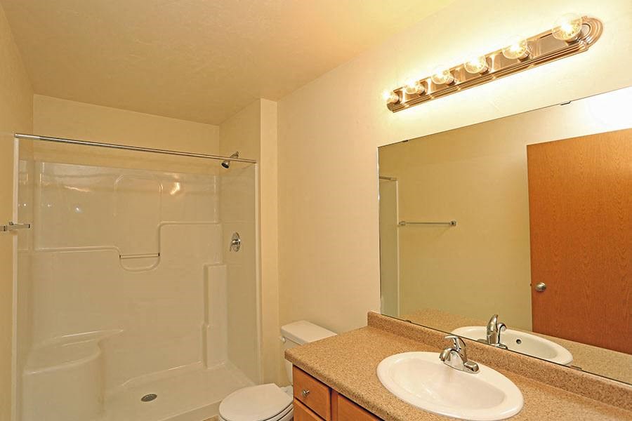 A bathroom with a toilet, sink, mirror and shower.