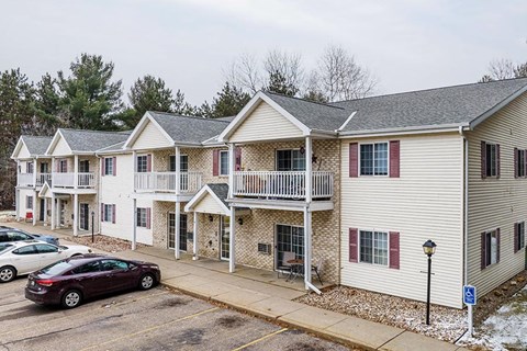 A parking lot with a car parked in front of a building with a balcony.