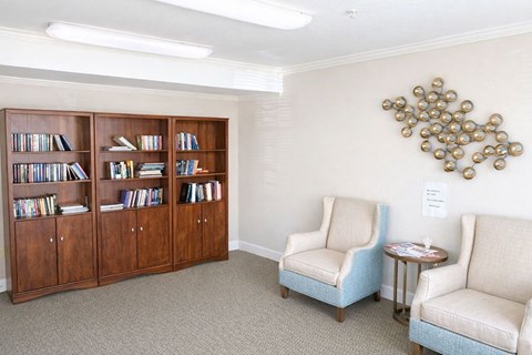 A room with a bookshelf, two chairs and a table.