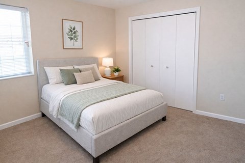 A bedroom with a bed, nightstand, and a plant.