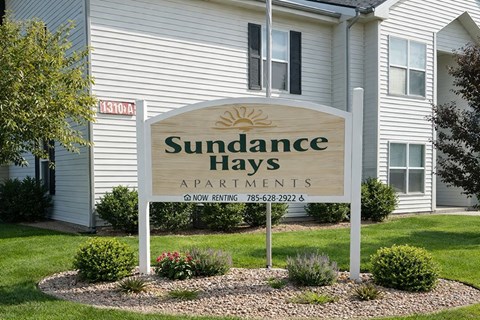A sign for Sundance Hays Apartments in front of a building.