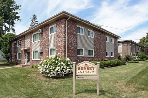 A Sunset Apartments sign is in front of a brick apartment building.