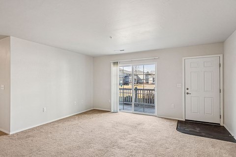 A white room with a carpeted floor and a sliding glass door leading to a balcony.
