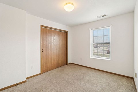 A room with a brown door and a window with a view of a fence and trees.