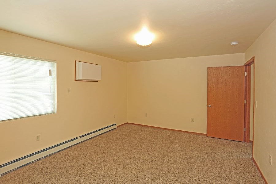 A room with a carpeted floor, a door, and a window with blinds.