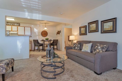 A living room with a grey couch, a glass coffee table, and a clock on the wall.