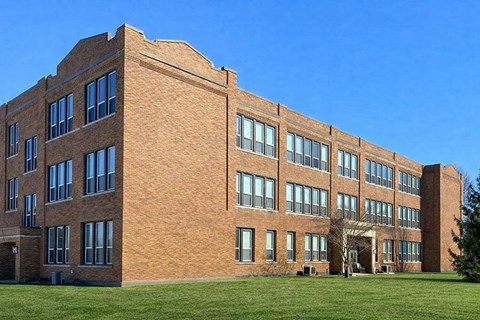 A large red brick building with many windows and a green lawn in front.