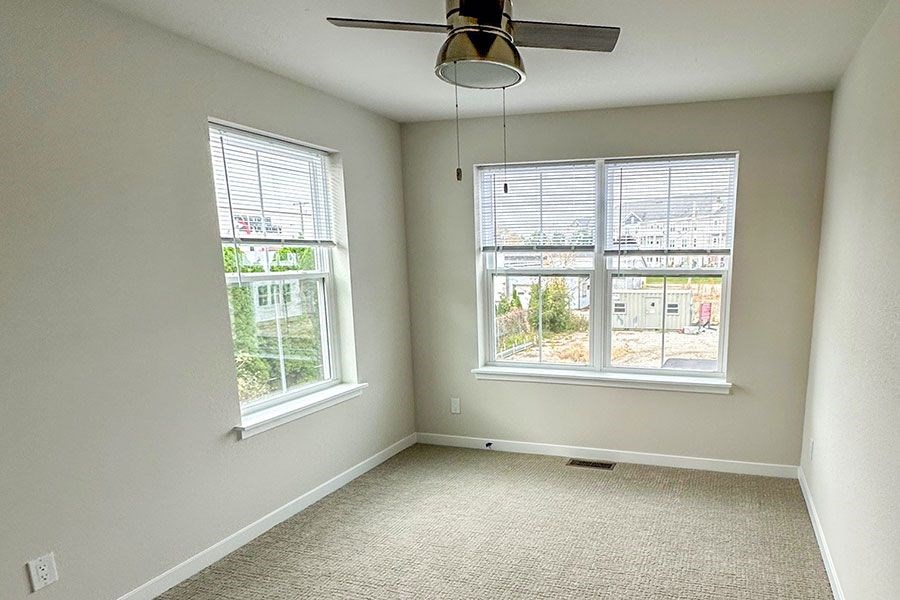 A room with a ceiling fan and two windows.