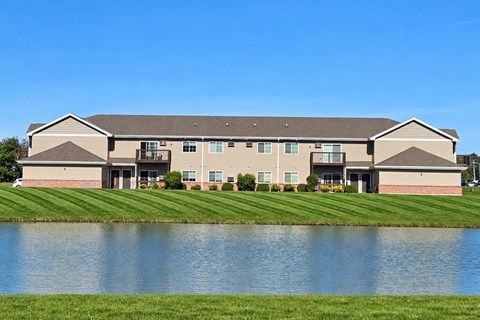 A large building with a grey roof and a pond in front.