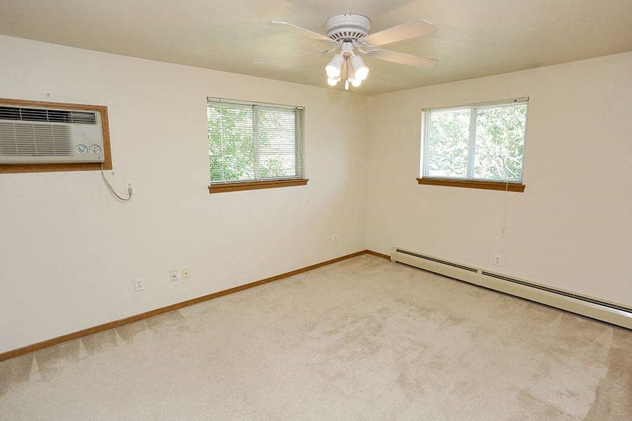 an empty room with a ceiling fan and two windows