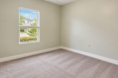 A room with a carpeted floor and a window showing a view of a house and trees.