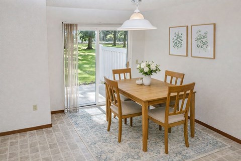 A dining room with a table and chairs and a view of a lawn outside.
