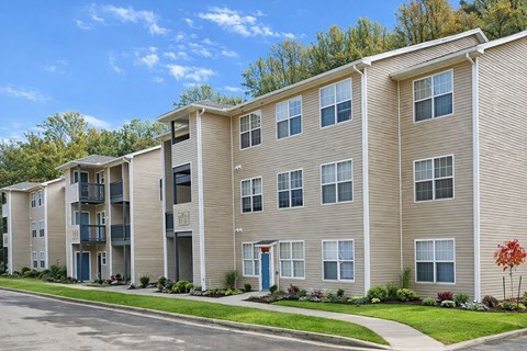 Apartment building with a blue door and a red tree in front.