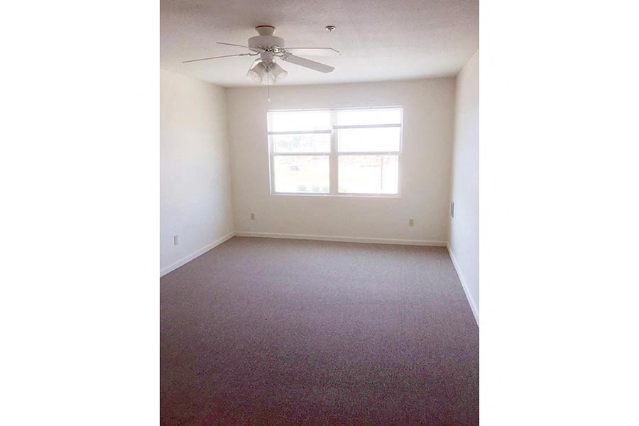 an empty living room with a ceiling fan and a window