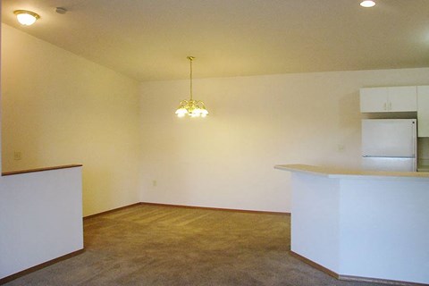 an empty living room with a kitchen and a chandelier
