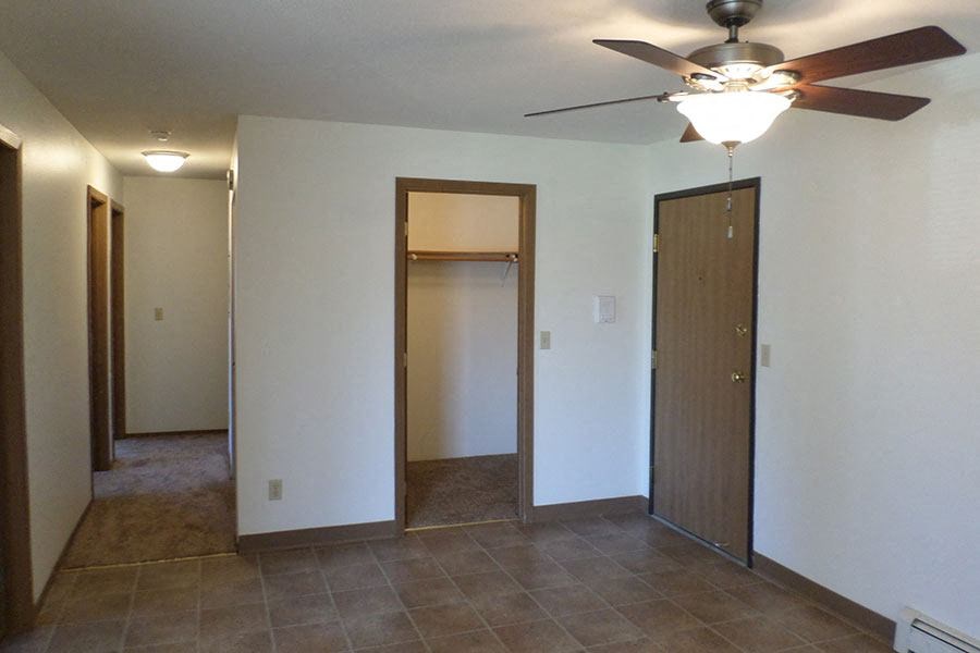an empty living room with a ceiling fan and a closet