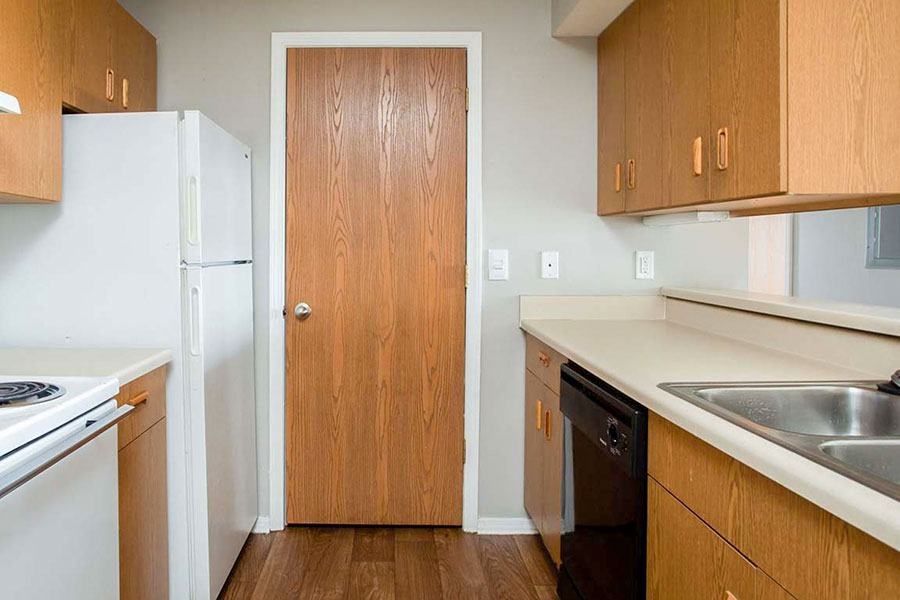 A kitchen with a white fridge, a wooden door, and a black dishwasher.