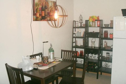 A dining room with a table, chairs, and a shelf with various items.