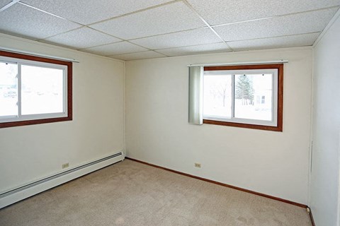 A room with a carpeted floor and two windows.