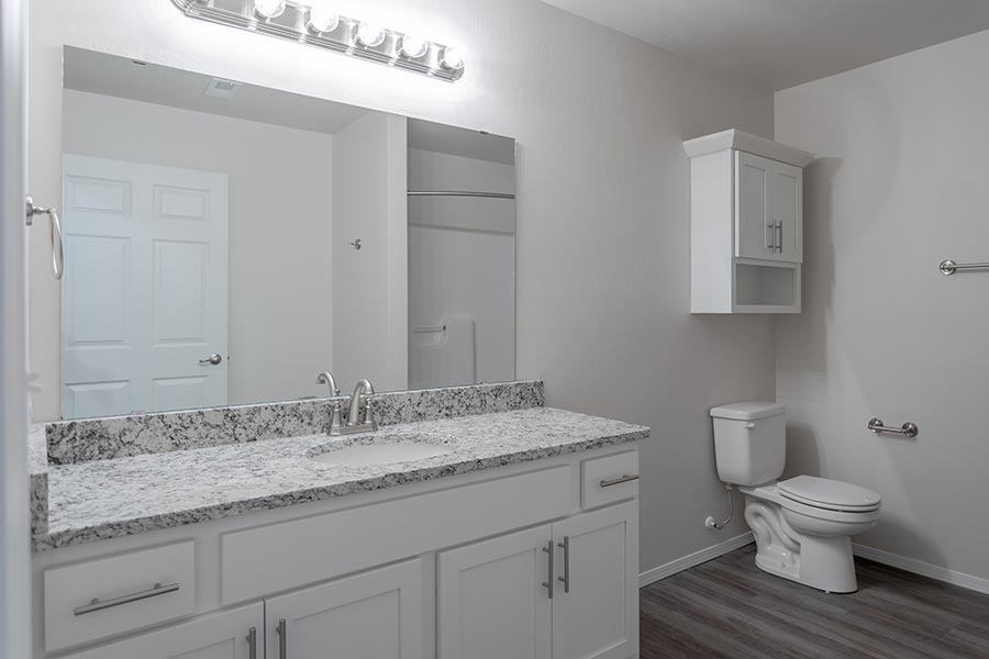 A white bathroom with a marble countertop and a toilet.