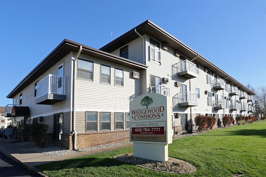 A sign for Wedgewood Commons leasing office in front of a building.