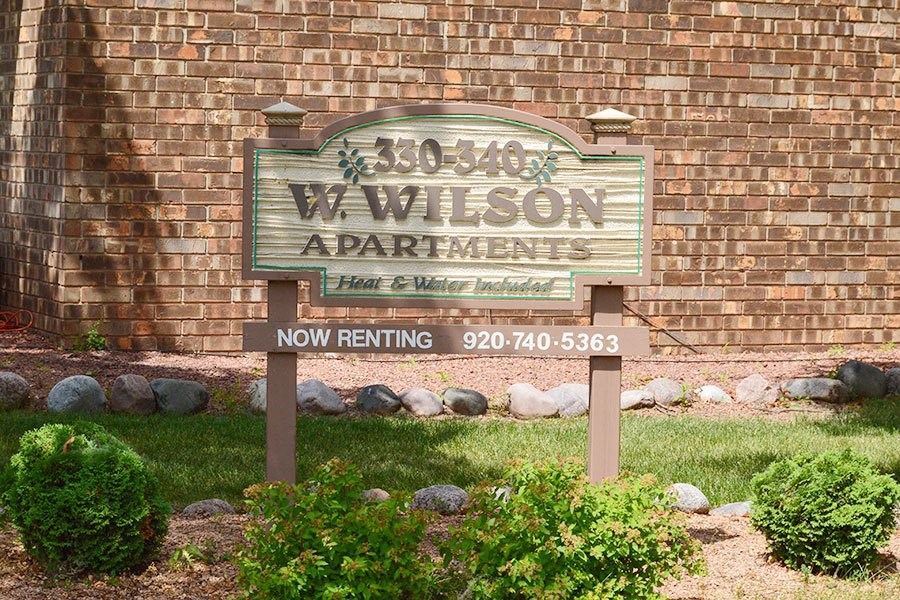 A sign for W. Wilson Apartments is displayed in front of a brick wall.