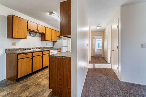 A kitchen with wooden cabinets and a carpeted hallway.