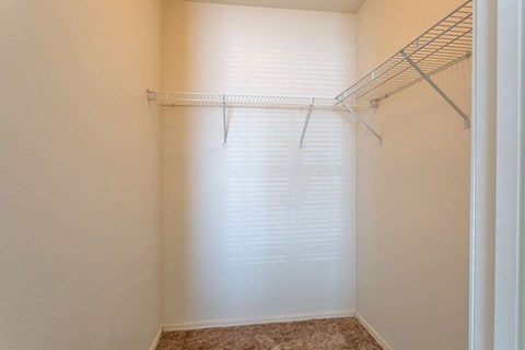 A white shelf is in the corner of a room with a window covered in blinds.