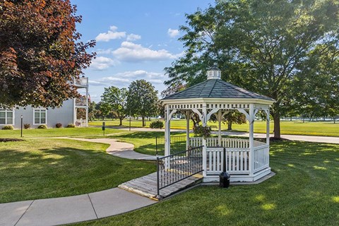 A gazebo with a white railing is surrounded by a green lawn.