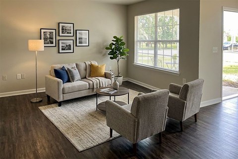 A living room with a grey couch, two chairs, and a table with a plant on it.
