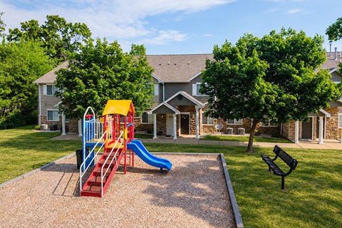 A playground with a slide and a bench in front of a house.