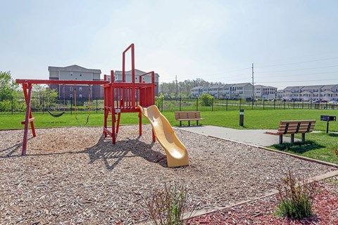 A playground with a red slide and a red swing set.