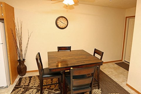 a dining room table with chairs and a clock on the wall