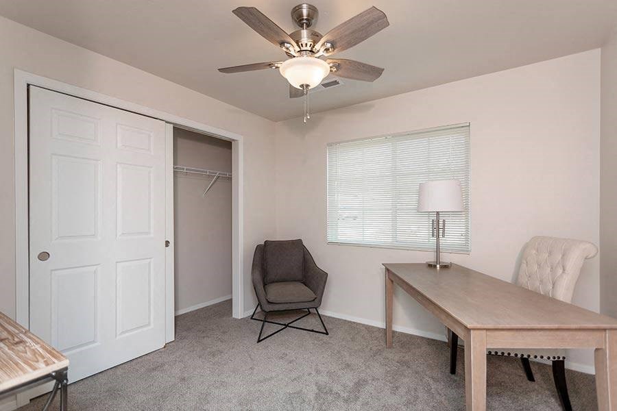 A room with a ceiling fan, a table, a chair, and a window with blinds.