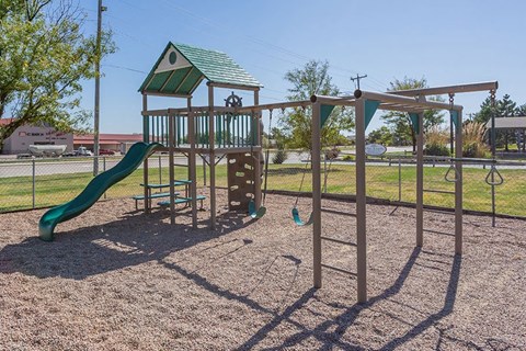 A playground with a green slide and a wooden swing set.