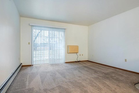 A room with a carpeted floor and a window with blinds.