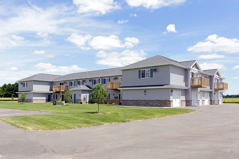 A large building with a grey roof and a parking lot in front.