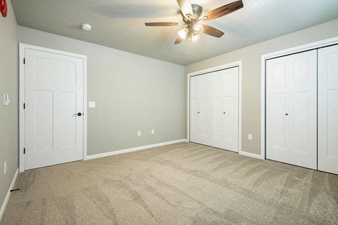 an empty bedroom with three doors and a ceiling fan